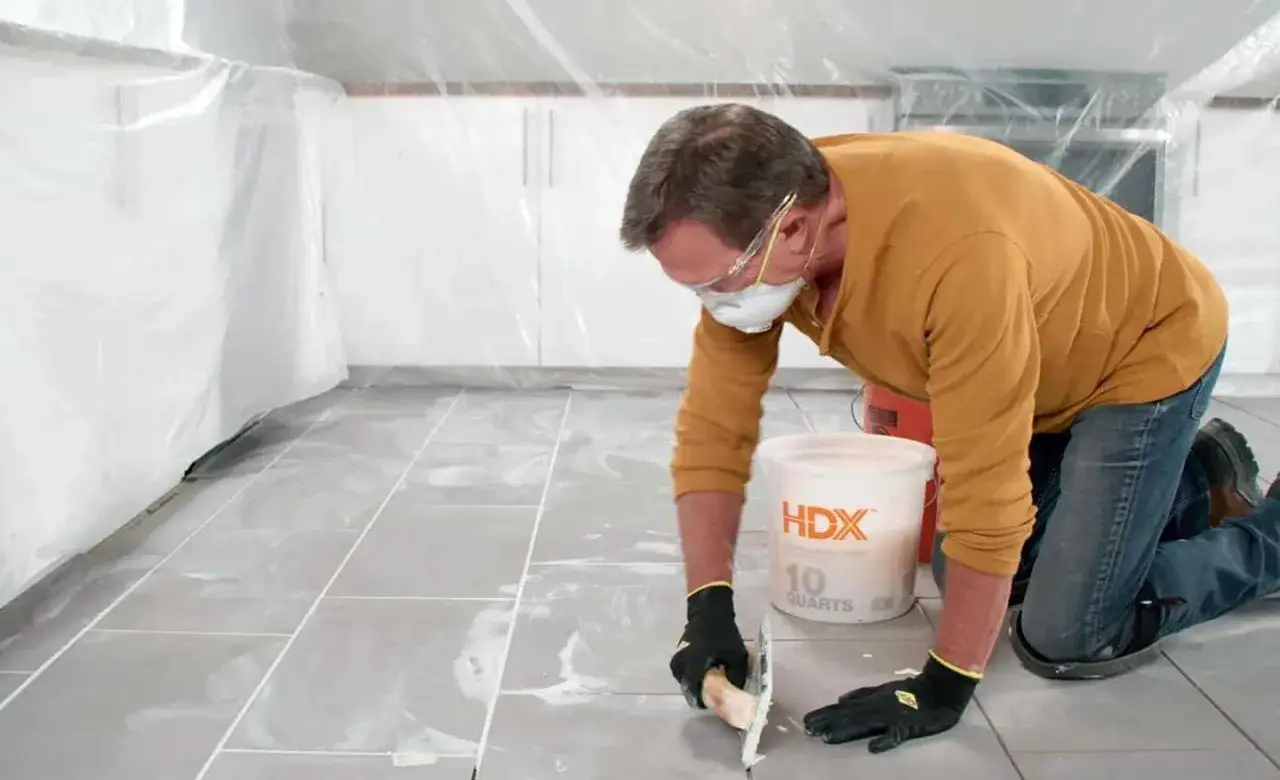 Un homme, prot&eacute;g&eacute;, applique du joint pour refaire le joint du carrelage.