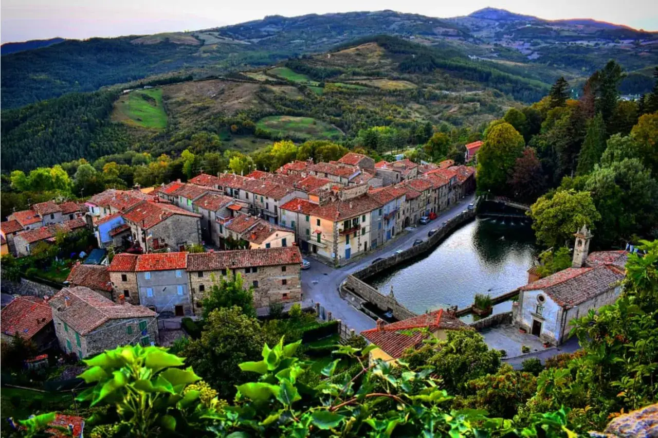 Vista dall'alto di Santa Fiora, con le case dai tetti rossi che si affacciano su un laghetto e colline verdi sullo sfondo.