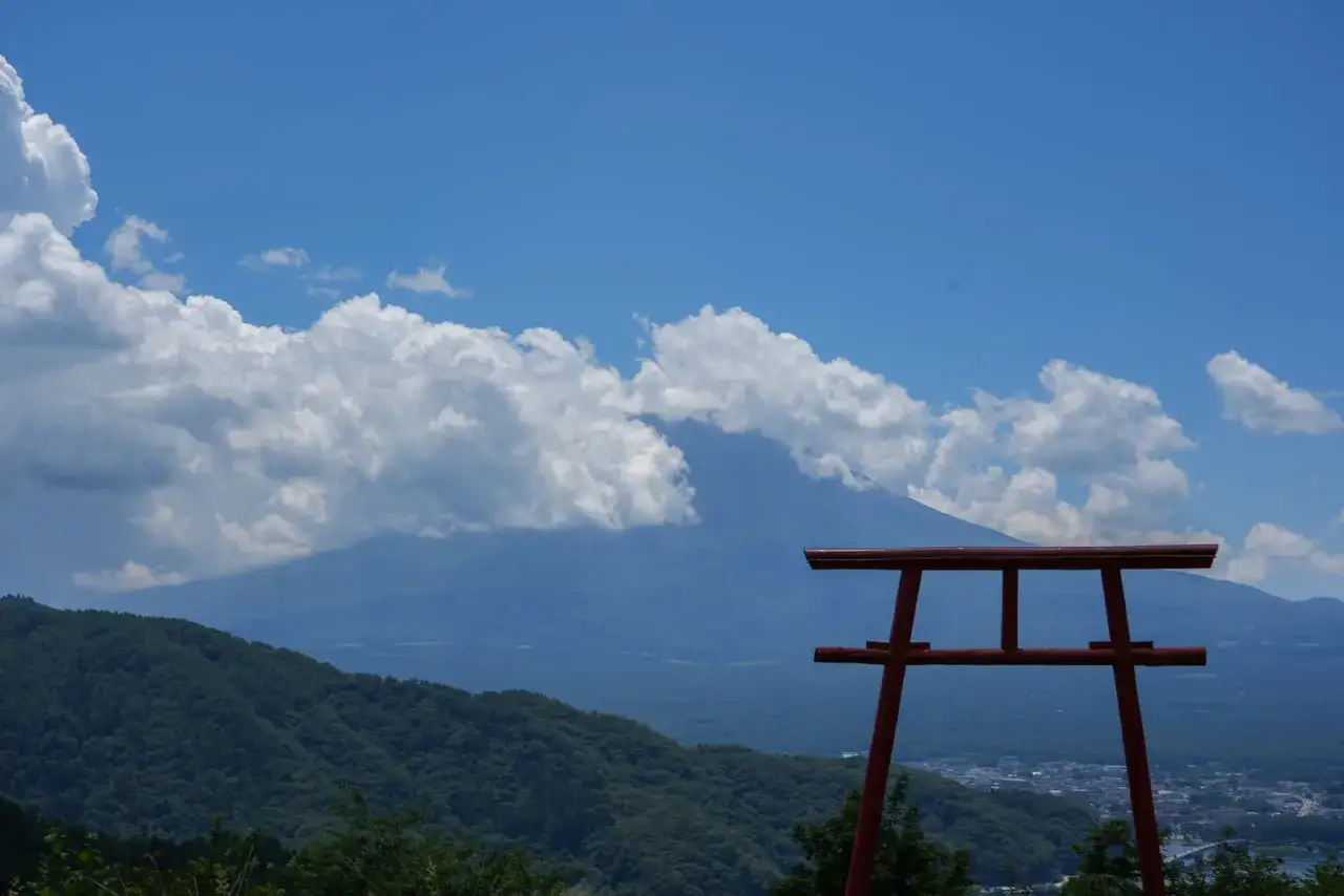Czerwona brama torii na tle góry Fudżi i chmur. Idealne miejsce na samodzielny wyjazd do Japonii.