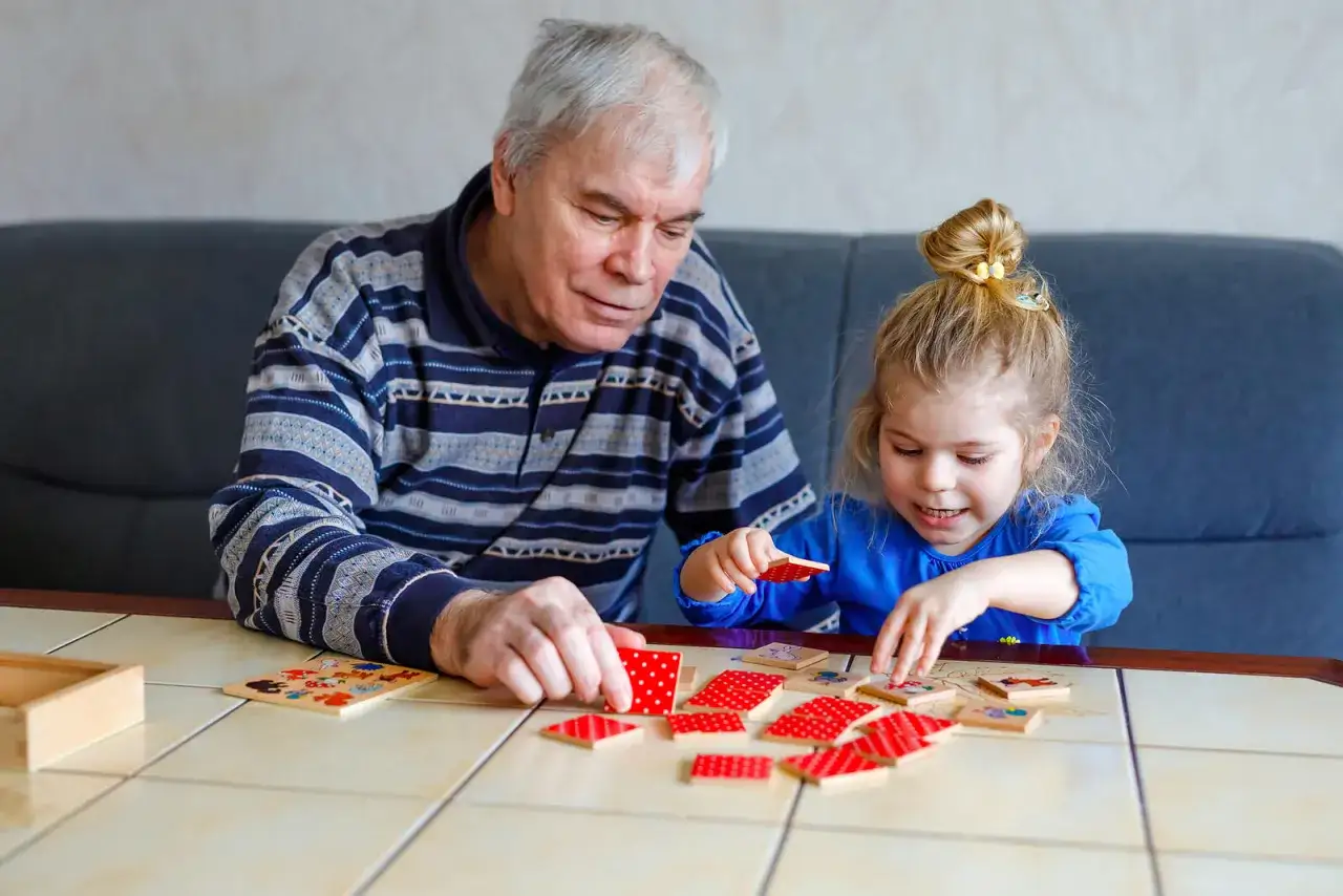 Abuelo y nieta jugando a un juego de memoria infantil con fichas de colores.