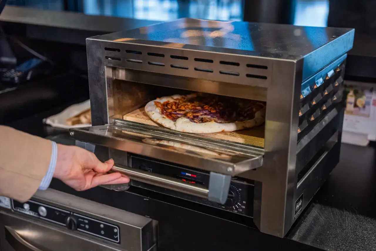 Main d'un homme ouvrant un four à pizza où cuit une pizza. Le début d'une belle aventure pour ouvrir une pizzeria.