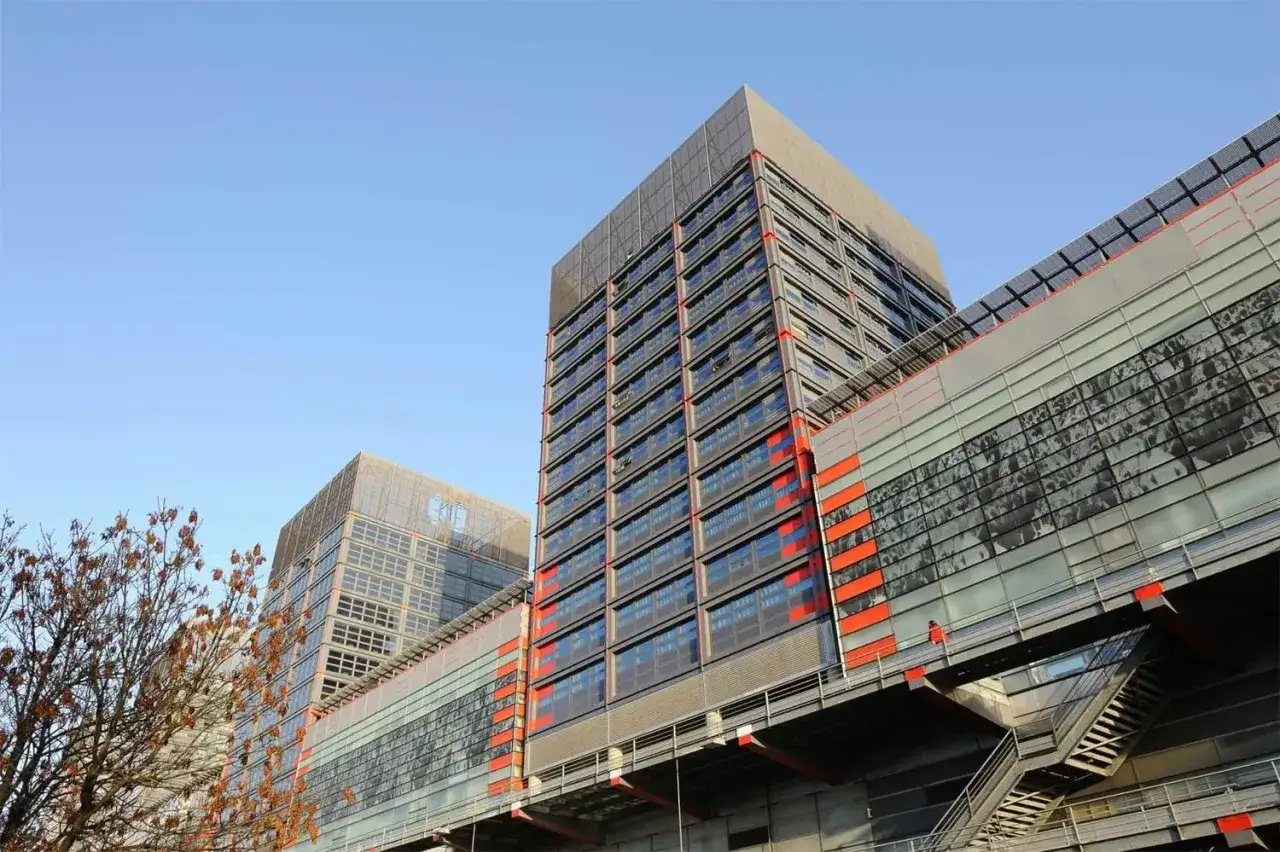 Edificios modernos con fachadas de cristal y detalles naranjas, como el **studea novalille**. Un árbol seco en primer plano.