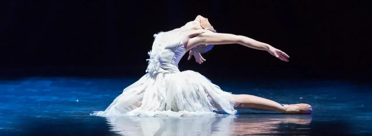 Ballerina in bianco, in una posa drammatica sul palco, evoca la magia del Lago dei Cigni a Roma.