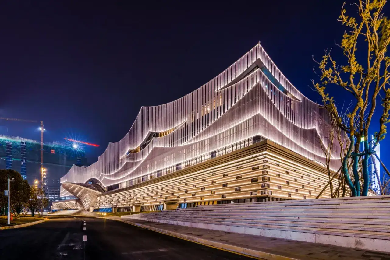 Nowoczesne oświetlenie budynku tworzy faliste, świetliste wzory na fasadzie, podkreślając jego architekturę.