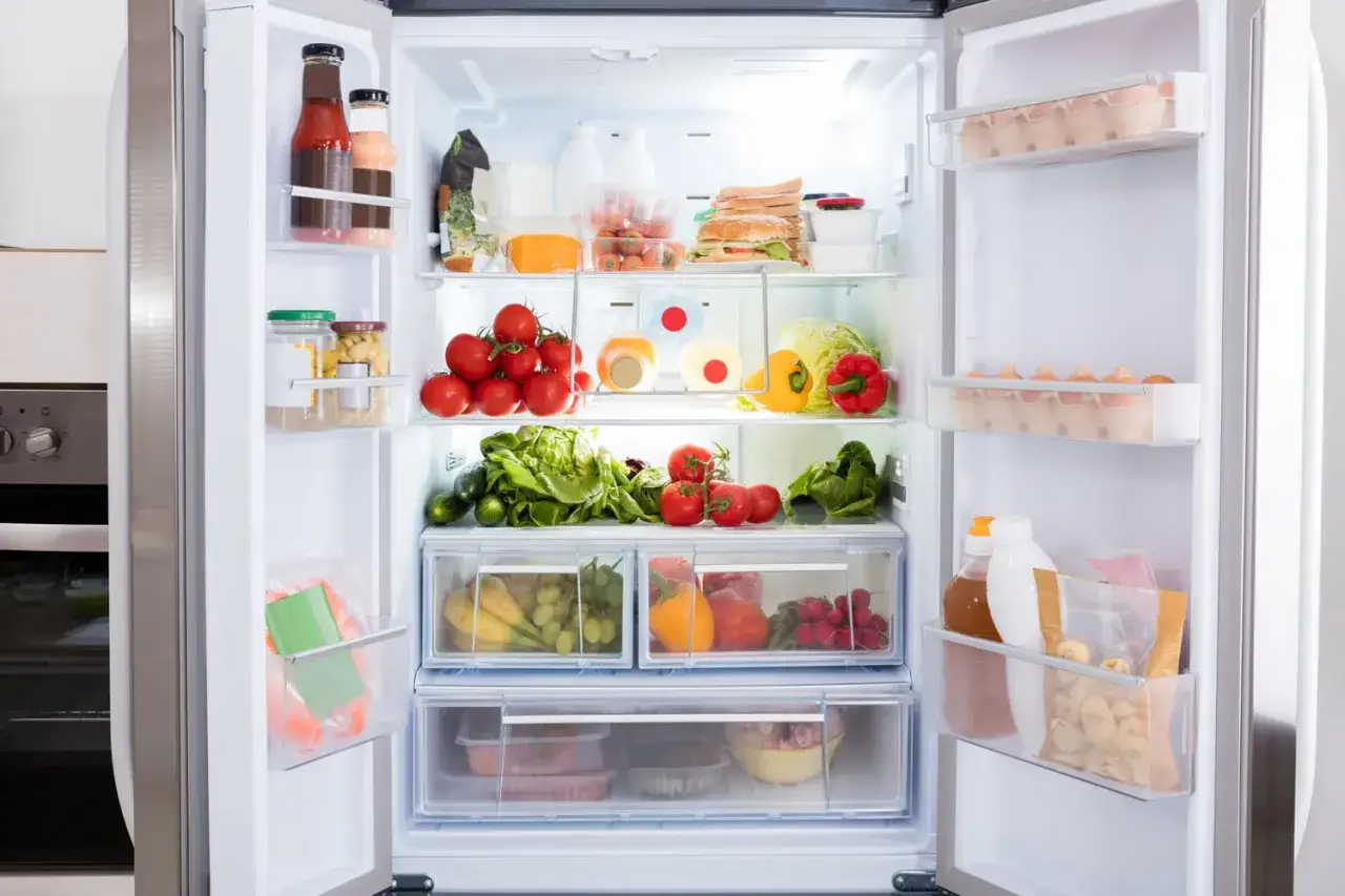 Un frigo bien rang&eacute;, pr&ecirc;t pour le nettoyage. Tomates, l&eacute;gumes verts, fruits et &oelig;ufs organis&eacute;s.
