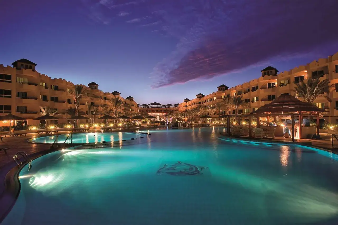 Wieczorem basen w Amwaj Blue Beach Resort & Spa, z podświetlaną wodą i palmami. Wiele pozytywnych amwaj blue beach resort & spa opinie.