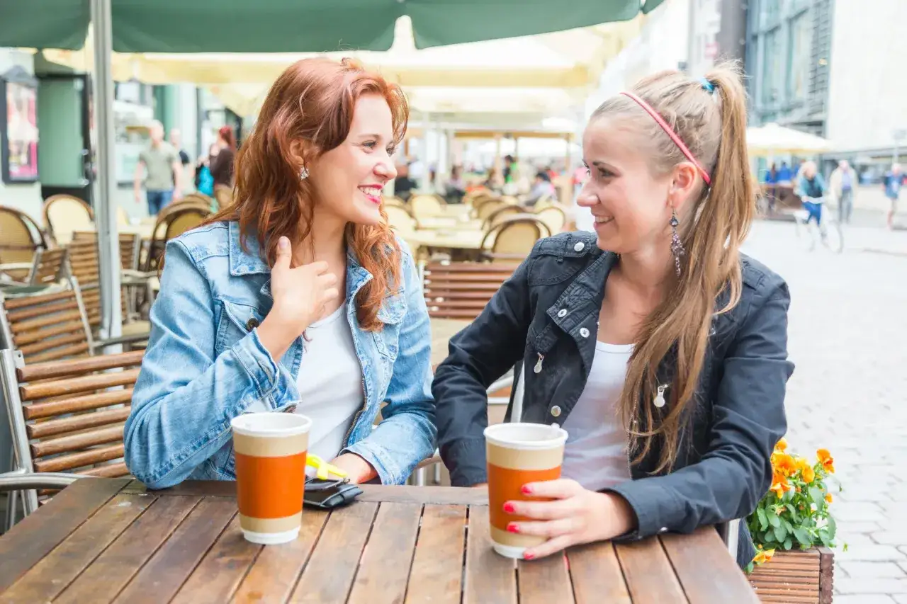 Dwie kobiety rozmawiają przy stoliku w kawiarni. To świetny sposób, jak poznać nowych ludzi i nawiązać przyjaźnie.