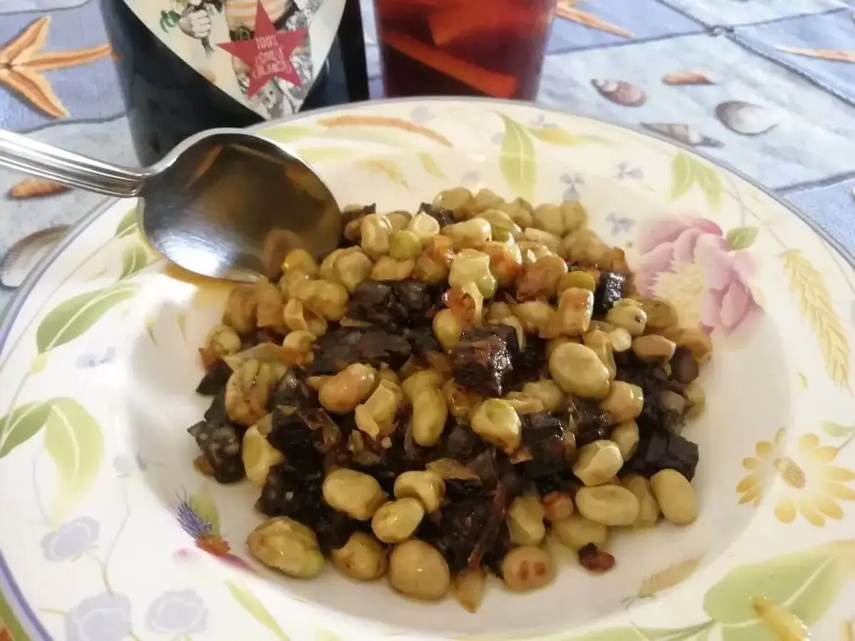 Plato de faves a la catalana con morcilla, acompa&ntilde;ado de una botella de vino y una copa de sangr&iacute;a.