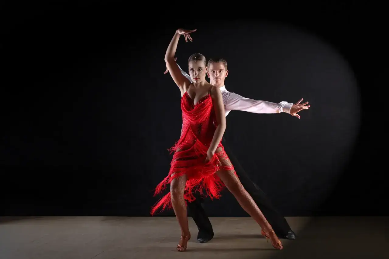 Coppia in abito rosso e bianco esegue una sensuale danza latina con movimenti aggraziati su sfondo scuro.