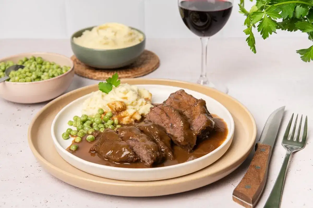 Carrilleras de ternera en salsa, un plato casero que evoca la receta de la abuela, servido con pur&eacute; de patatas y guisantes.