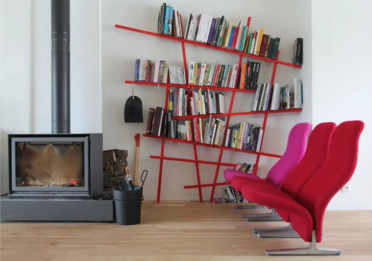 Camino acceso, attrezzi da camino, e moderne piccole librerie rosse piene di libri, con sedie colorate.
