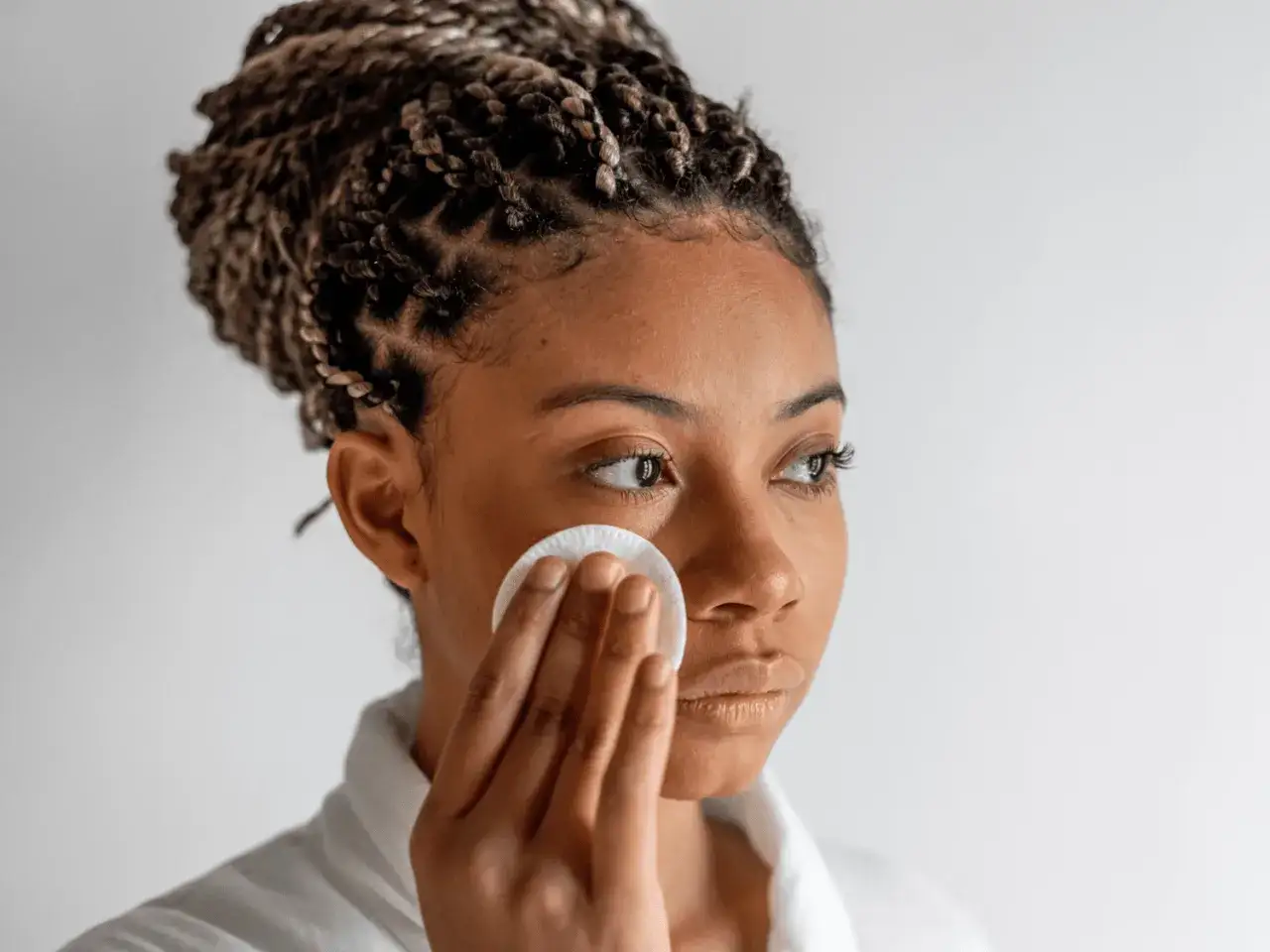 Donna con treccine applica tonico viso con dischetto di cotone. Scopri a cosa serve il tonico viso per una pelle fresca.