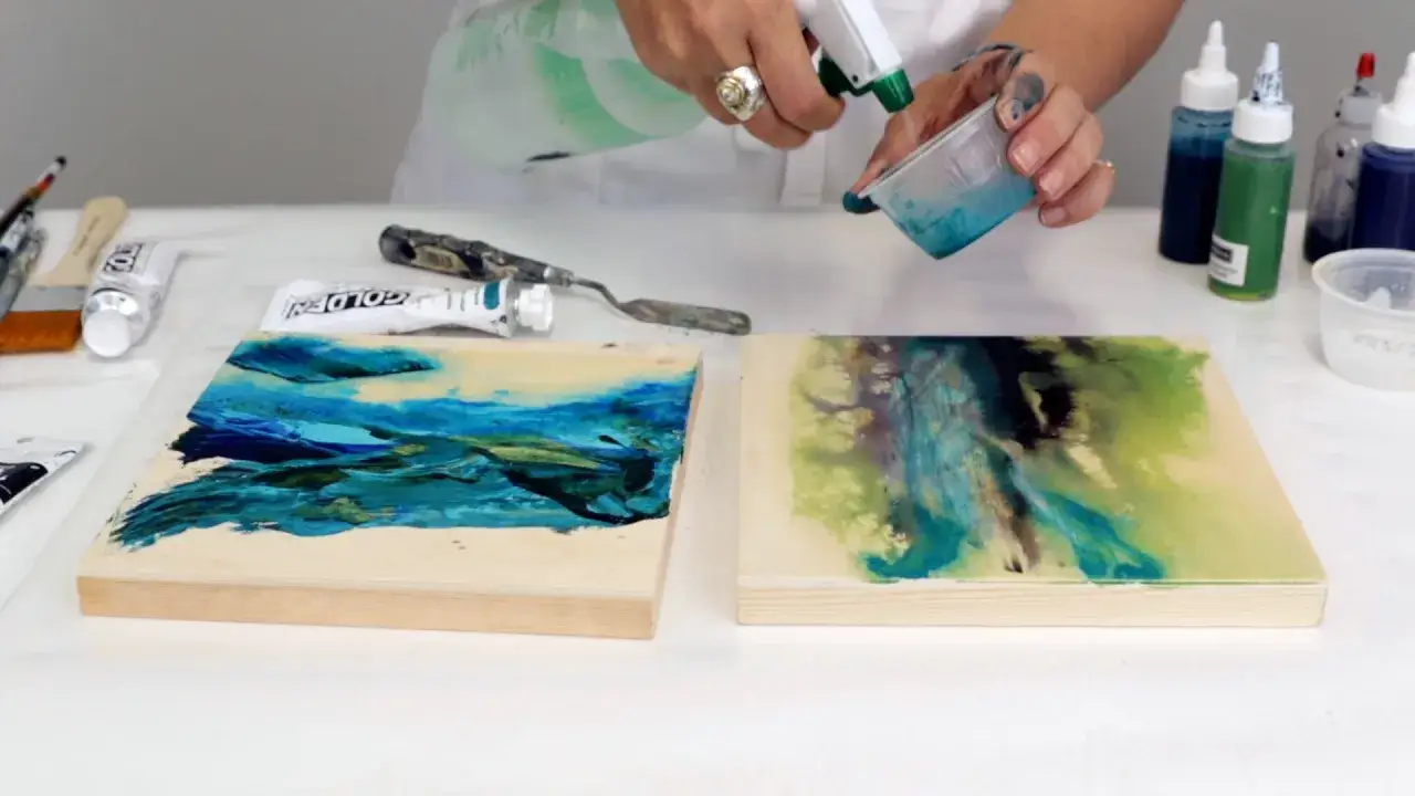 Mani che creano arte: si sta colorando la resina con acrilici, creando effetti fluidi e vibranti su due piccole tele di legno.