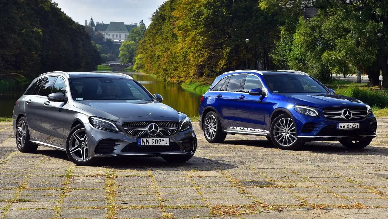 Dwa modele Mercedes-Benz: eleganckie kombi i sportowy SUV, zaparkowane nad wodą, na tle jesiennych drzew i pałacu.