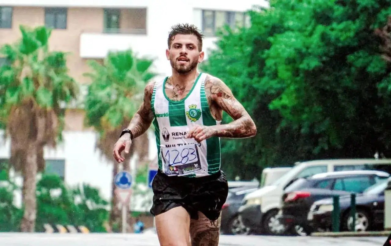 Mężczyzna z tatuażem bieganie, w koszulce sportowej, podczas zawod&oacute;w.