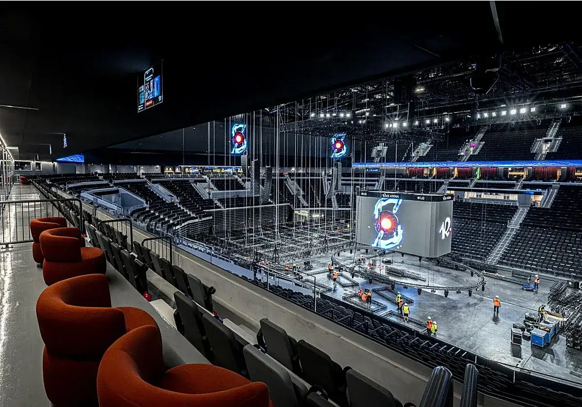 Interior de la Roig Arena, con asientos vacíos y trabajadores preparando el escenario para un evento.