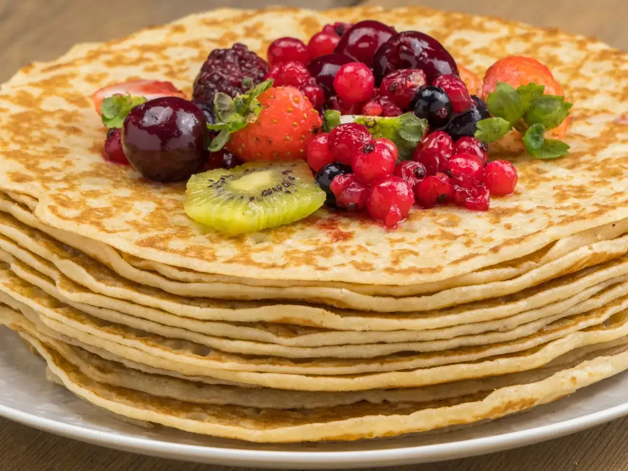 Pila de crepes doradas, cubiertas con frutos rojos frescos y una rodaja de kiwi. Una deliciosa receta crepes para disfrutar.