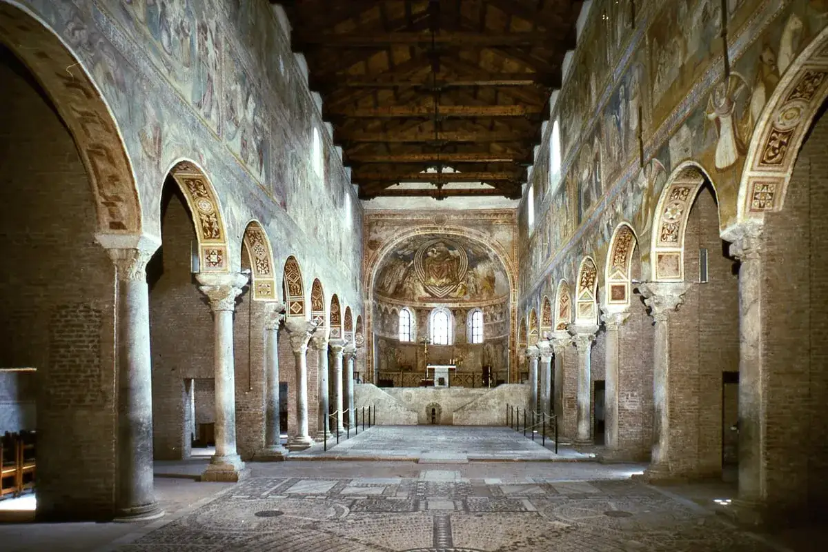 Interno di un'antica basilica, uno dei santuari dell'Emilia Romagna, con affreschi sulle pareti, colonne imponenti e un mosaico sul pavimento.