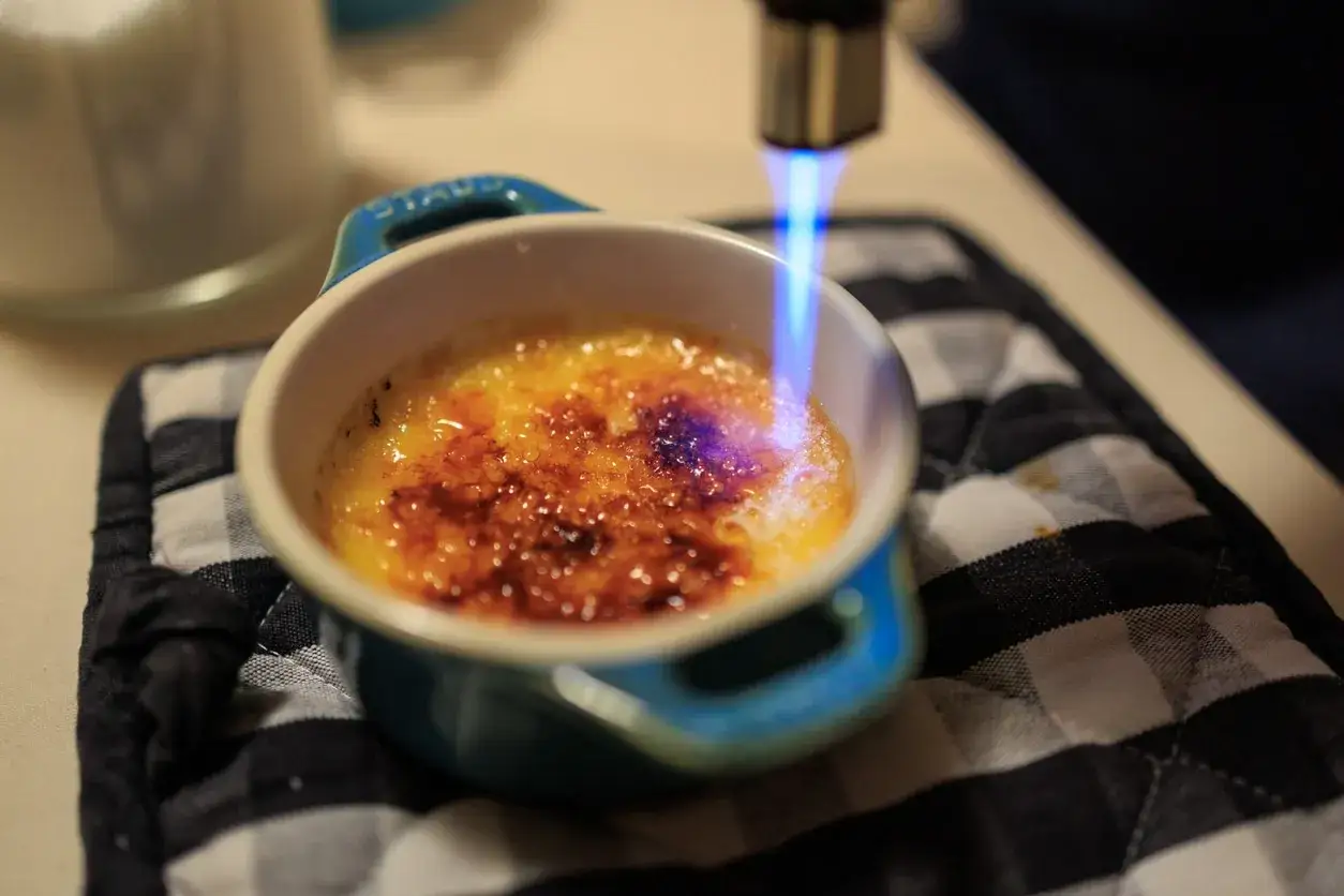 La flamme d'un chalumeau caramélise le sucre d'une crème brûlée, rappelant son origine française.