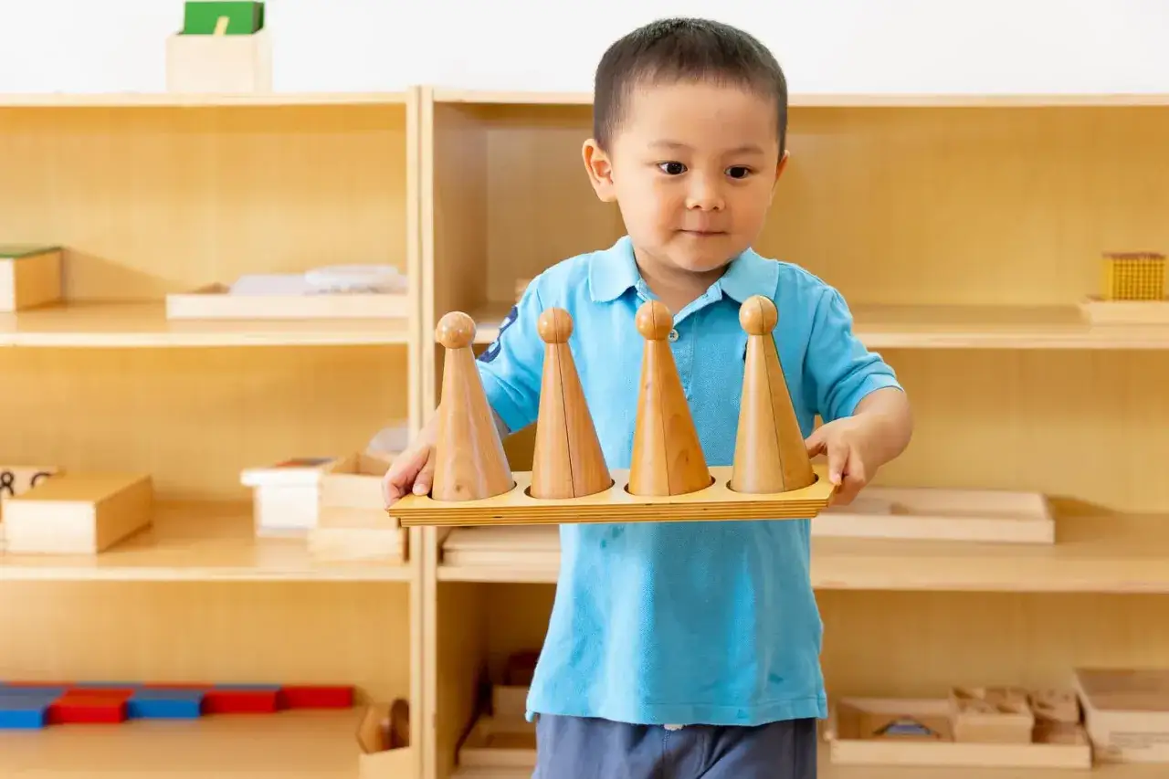 Chłopiec w niebieskiej koszulce trzyma drewniane stożki, ćwicząc metodę Montessori.