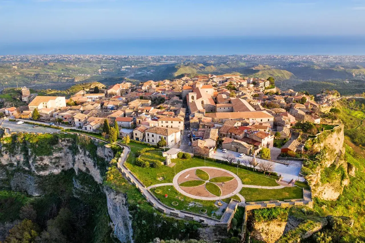 Panoramica aerea di un pittoresco borgo arroccato su una scogliera, uno dei tanti **borghi da visitare in Calabria**, con case in pietra e tetti rossi che si affacciano sul mare.