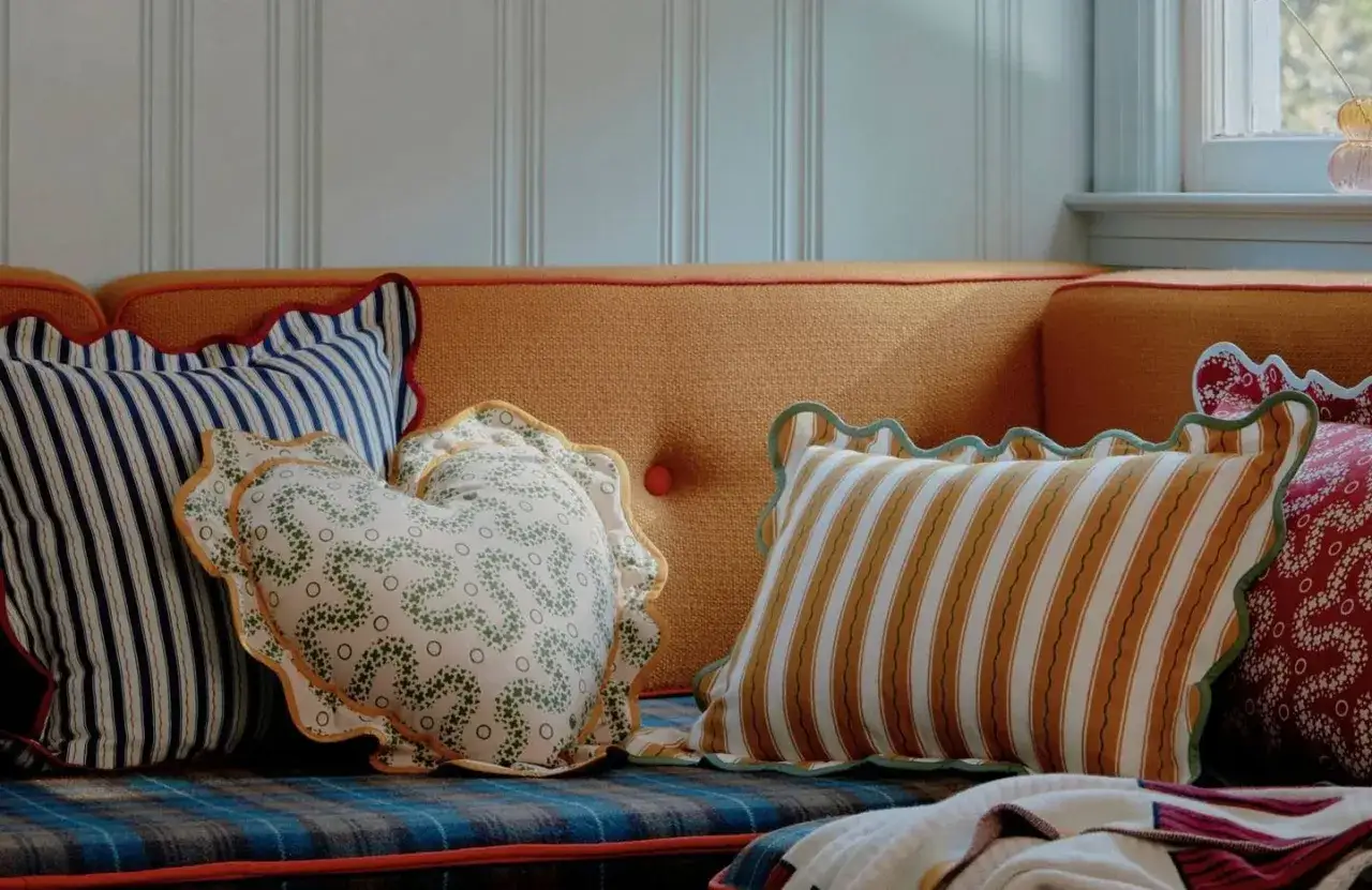 Plusieurs coussins aux motifs vari&eacute;s, dont un en forme de c&oelig;ur, d&eacute;corent un canap&eacute; orange. Le **taille coussin** est parfait pour un confort douillet.