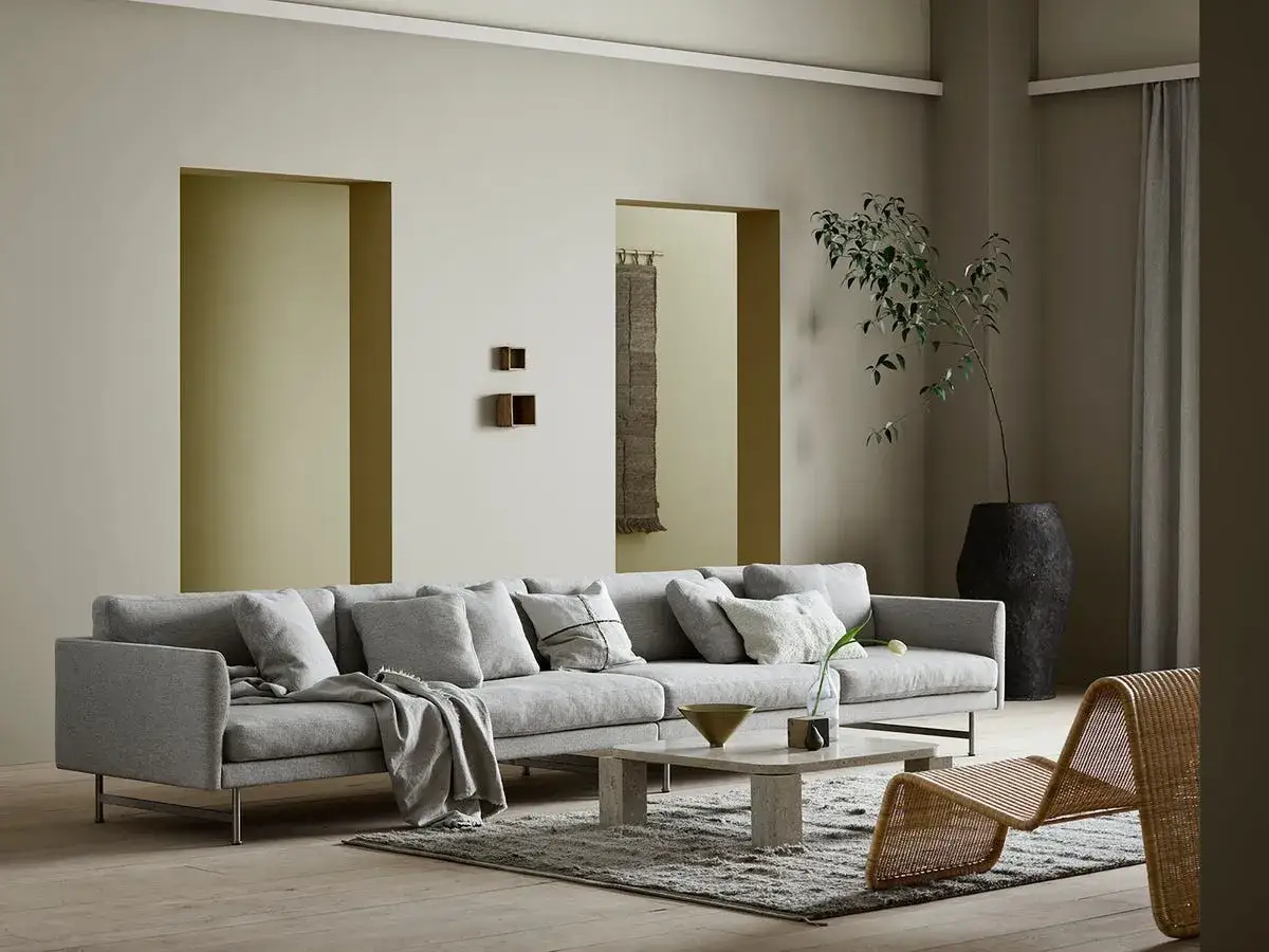 Sof&aacute; gris, mesa de centro de m&aacute;rmol y silla de mimbre en una sala de estar moderna. La pared tiene un color neutro, ideal para pintar casa.