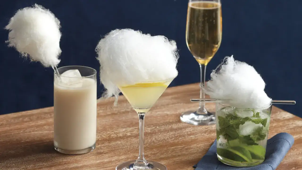 Trzy drinki z watą cukrową: biały koktajl, martini z cytryną i mojito. Obok kieliszek szampana.