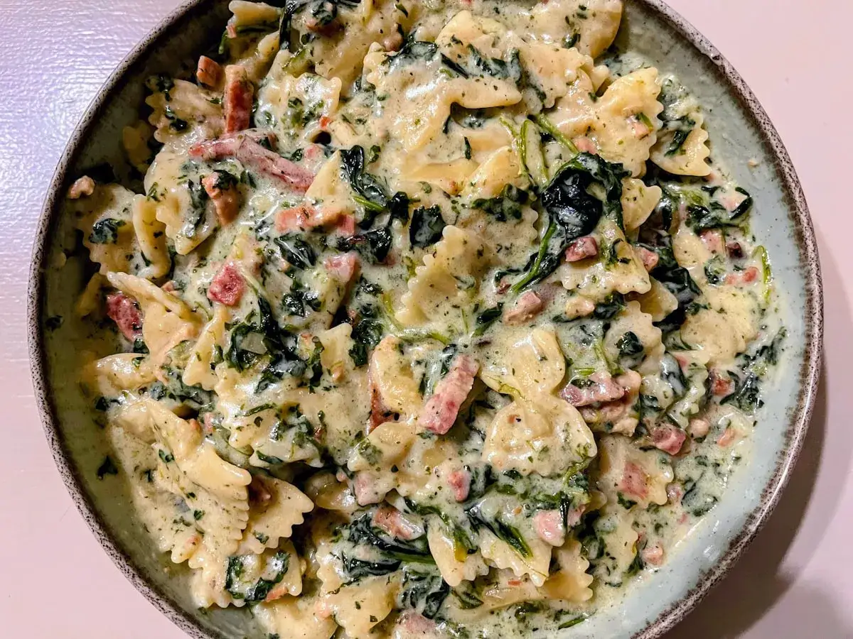 Pyszny makaron farfalle w kremowym sosie ze szpinakiem mrożonym i kawałkami boczku.
