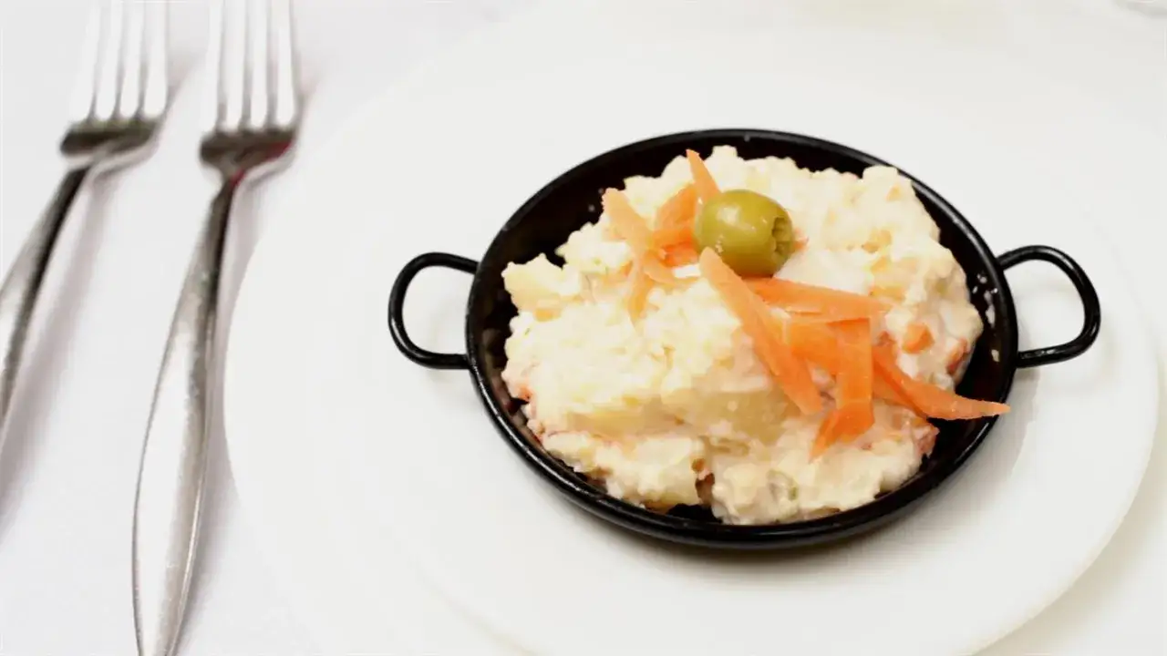 Ensaladilla rusa andaluza in a black bowl, garnished with shredded carrots and an olive. Two forks are visible on the left.