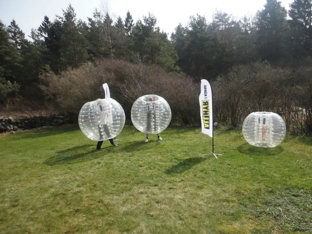 Tre personer i stora genomskinliga bollar redo f&ouml;r bumperball hyra. En flagga med texten 