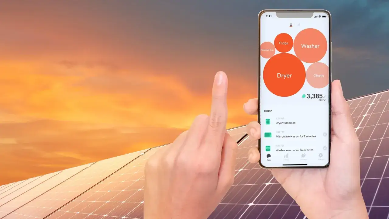 En hand håller upp en mobil med sesol appen som visar energiförbrukning från torktumlare, tvättmaskin och ugn. Solpaneler syns i bakgrunden.