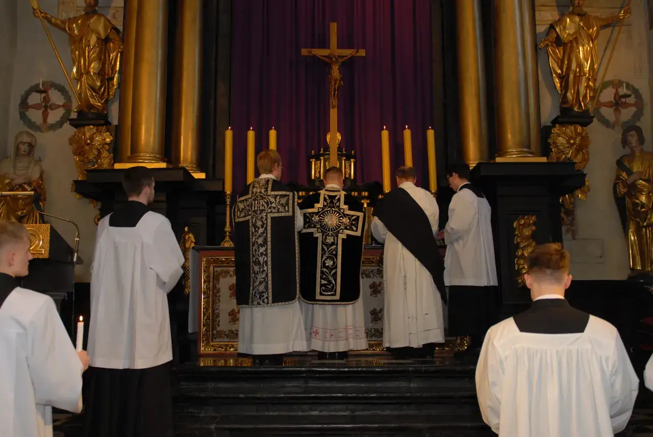 Uroczysta liturgia Męki Pańskiej w kościele. Klerycy w strojach liturgicznych stoją przed ołtarzem.