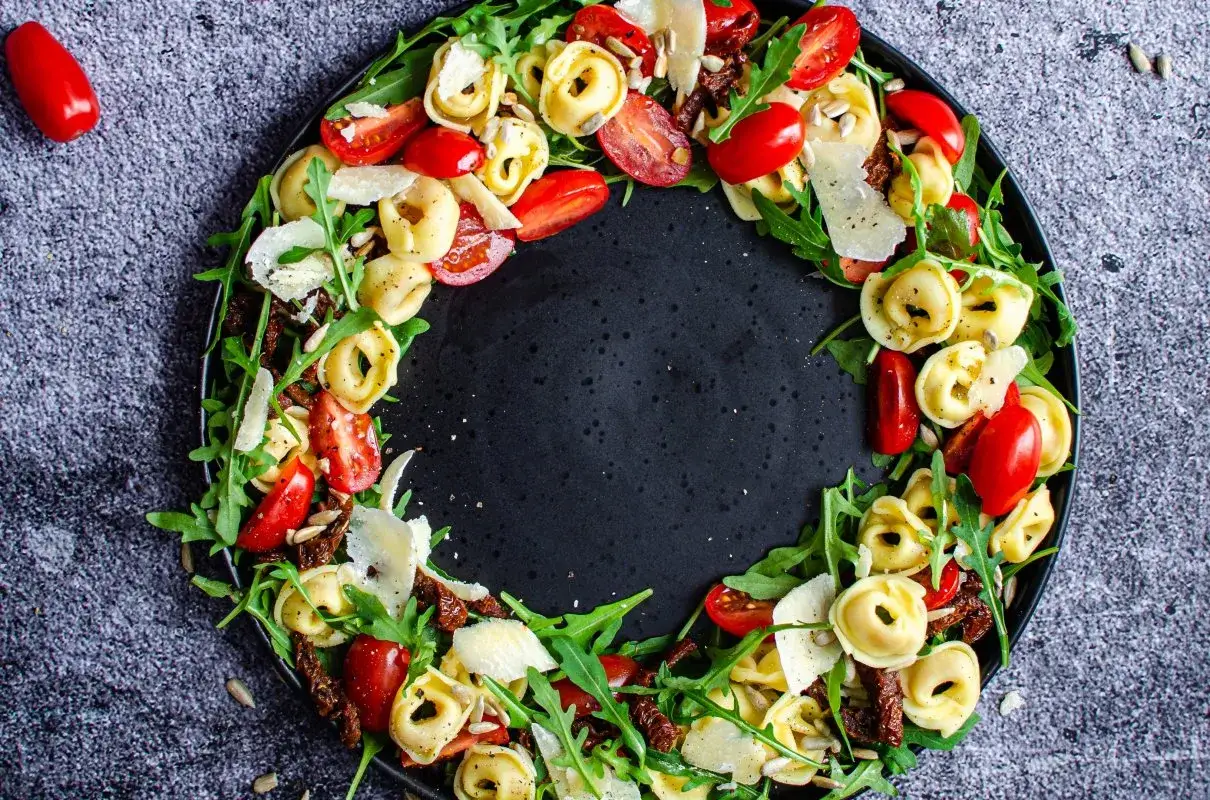 Kolorowa sałatka z tortellini, pomidorkami koktajlowymi, rukolą i parmezanem, ułożona na czarnym talerzu.