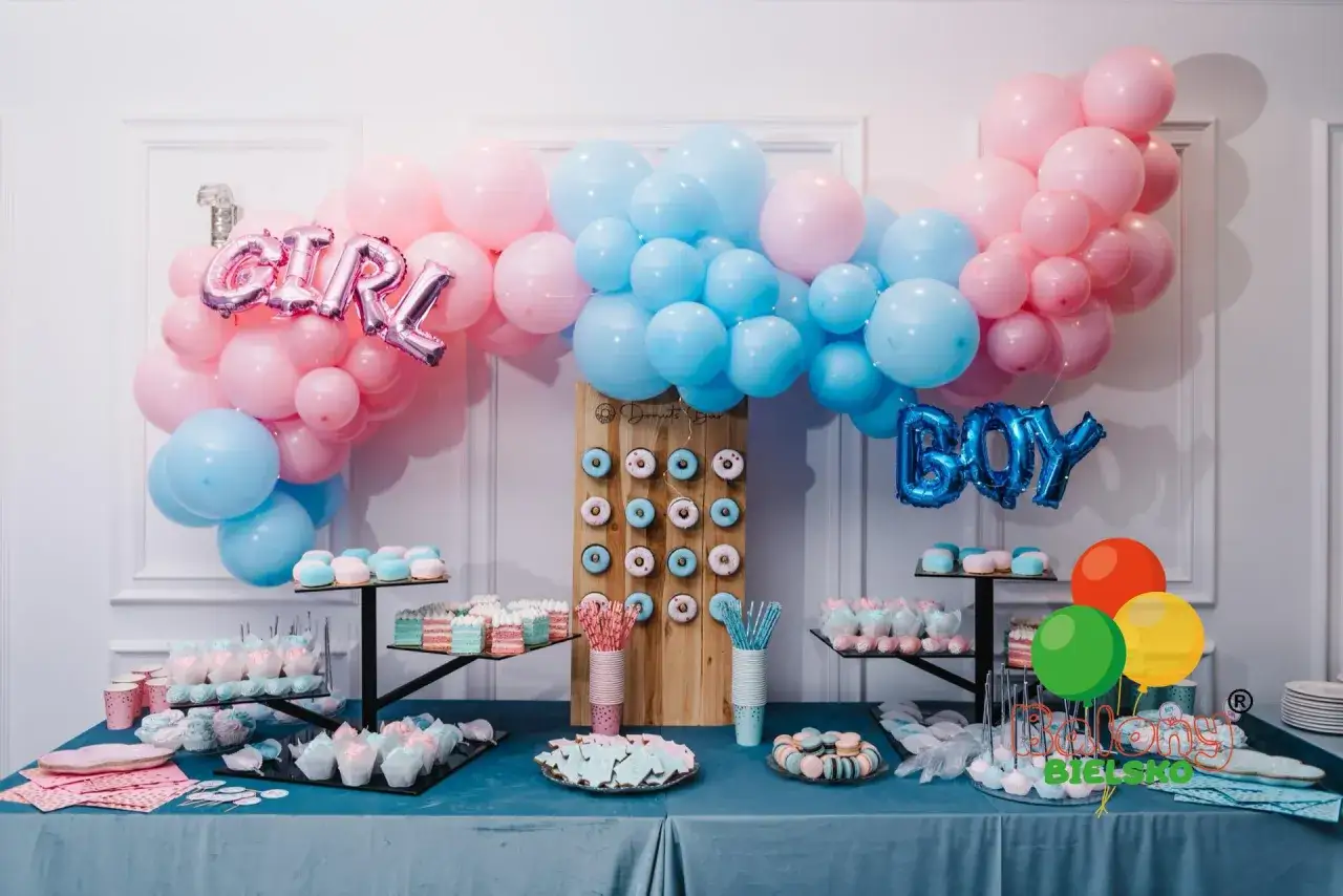 Uroczy stół z przekąskami na przyjęcie gender reveal. Balony w kolorach różowym i niebieskim, babeczki, pączki i ciasteczka.
