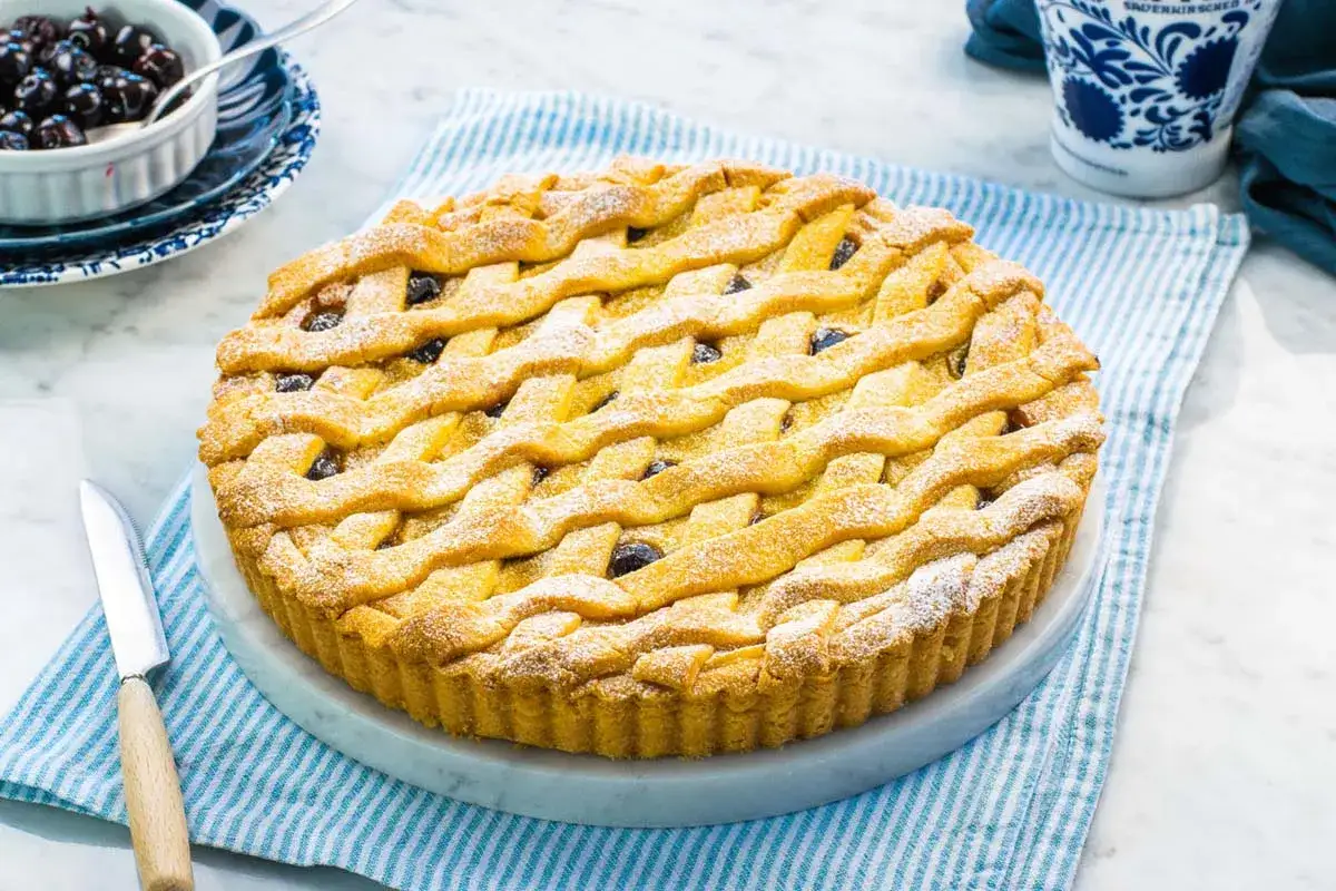 Deliziosa crostata amalfitana con ripieno di amarene, decorata con una griglia di pasta frolla e spolverata di zucchero a velo.