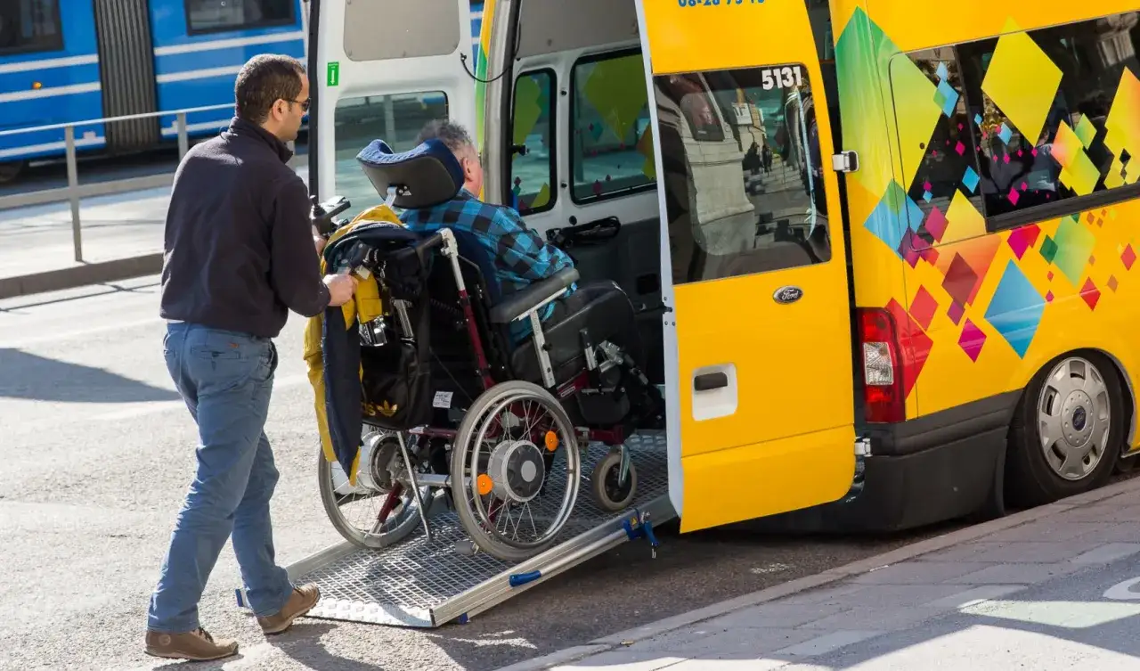 Opiekun pomaga osobie na wózku inwalidzkim wsiąść do żółtego busa. Czy opiekun osoby niepełnosprawnej płaci za bilet?