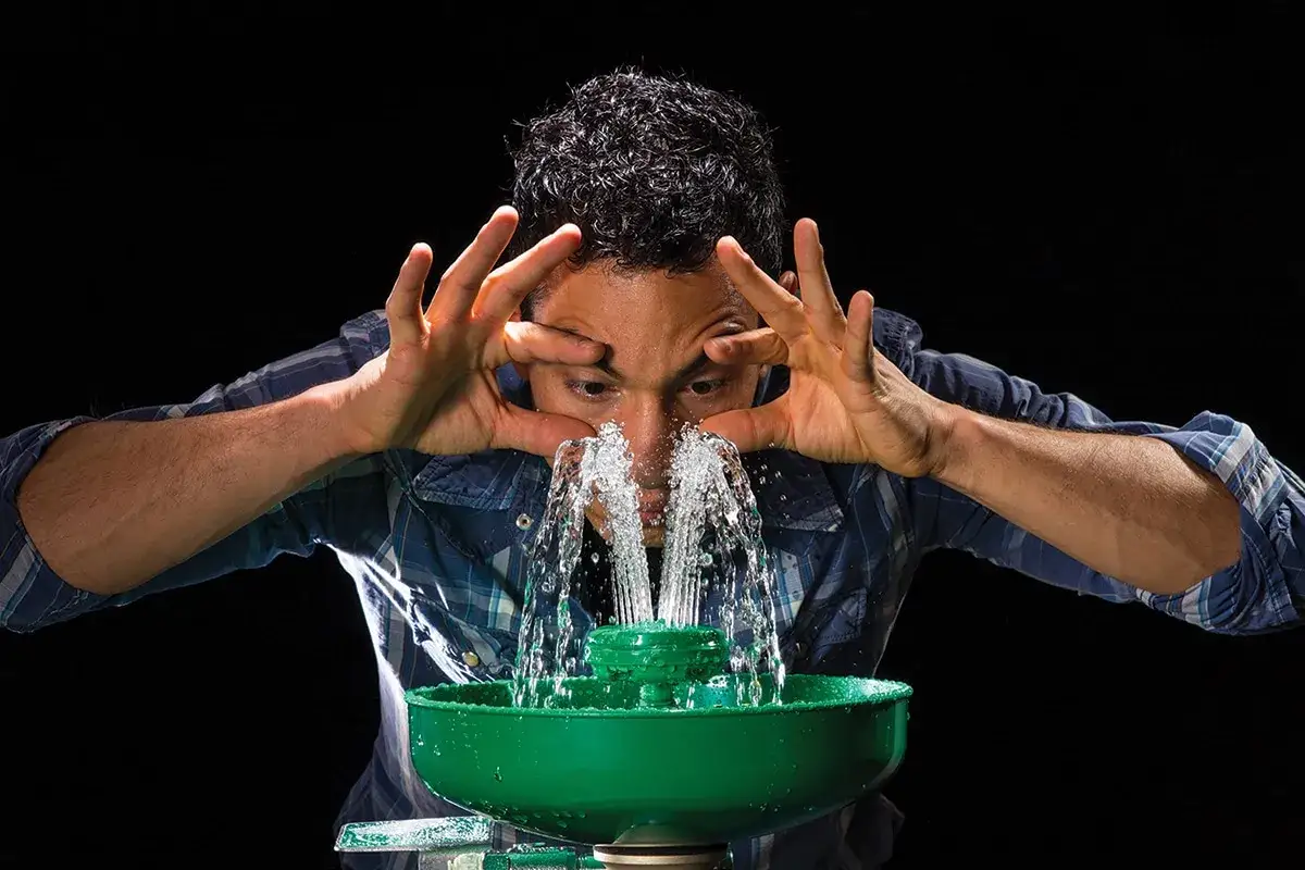 Uomo con shampoo negli occhi congiuntivite, si lava il viso con una fontanella d'emergenza.