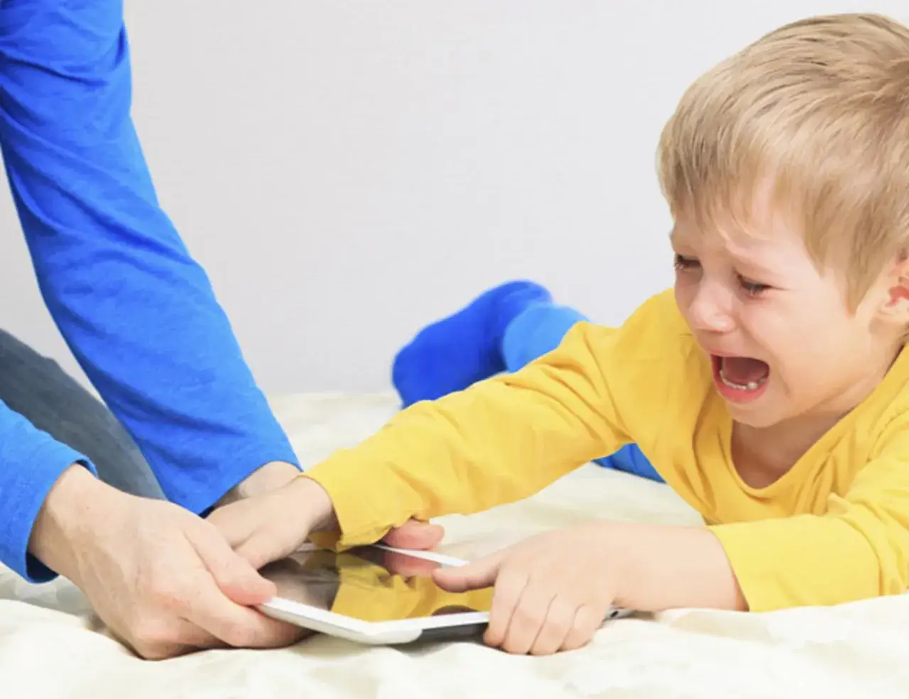Un ni&ntilde;o llora desconsoladamente mientras un adulto le quita una tablet. Expresi&oacute;n de fuertes emociones ni&ntilde;os.