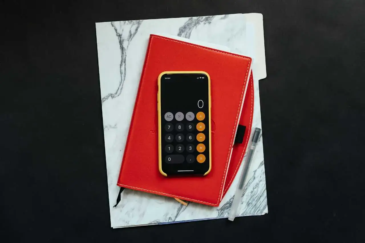 Tel&eacute;fono con calculadora sobre libreta roja y m&aacute;rmol. Preparando un asiento contable de un gasto sin factura.