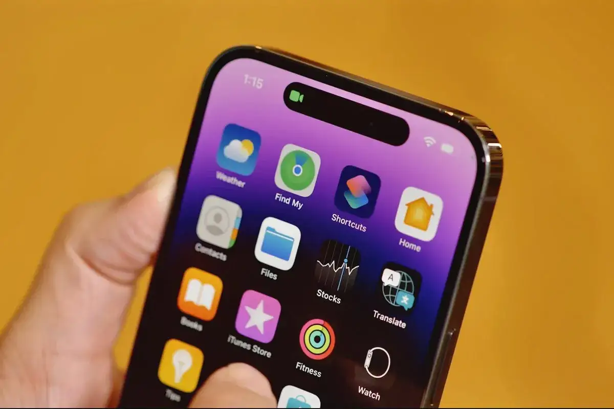Dłoń trzyma iPhone'a z widoczną dynamiczną wyspą, na ekranie ikony aplikacji.