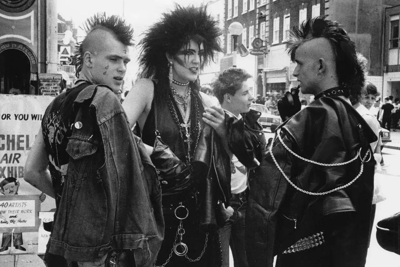 Młodzi ludzie z irokezami i w sk&oacute;rzanych kurtkach, uosabiający punk subkulturę, rozmawiają na ulicy.