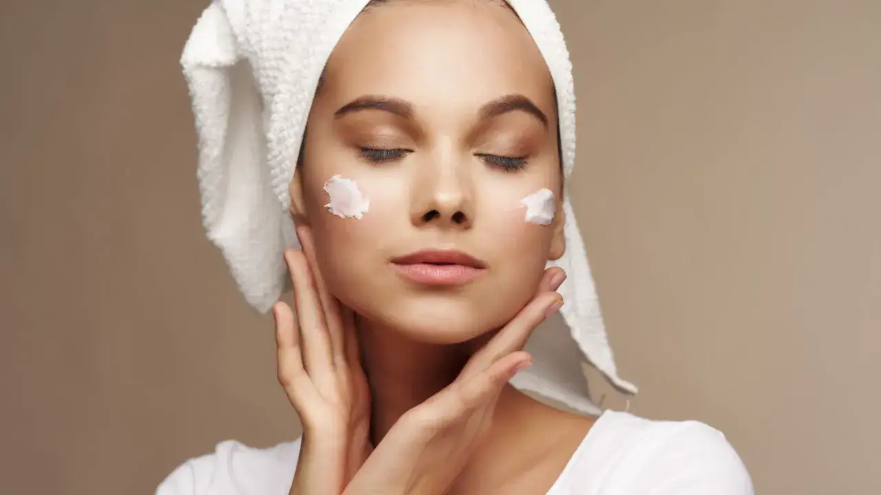 Mujer con toalla en la cabeza y crema en las mejillas, cuidando su piel con productos de atida mifarma.