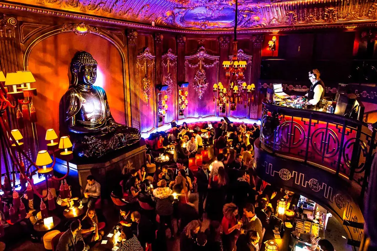 Una statua di Buddha domina la pista da ballo di una discoteca a Montecarlo, con gente che balla e DJ che mixa musica.