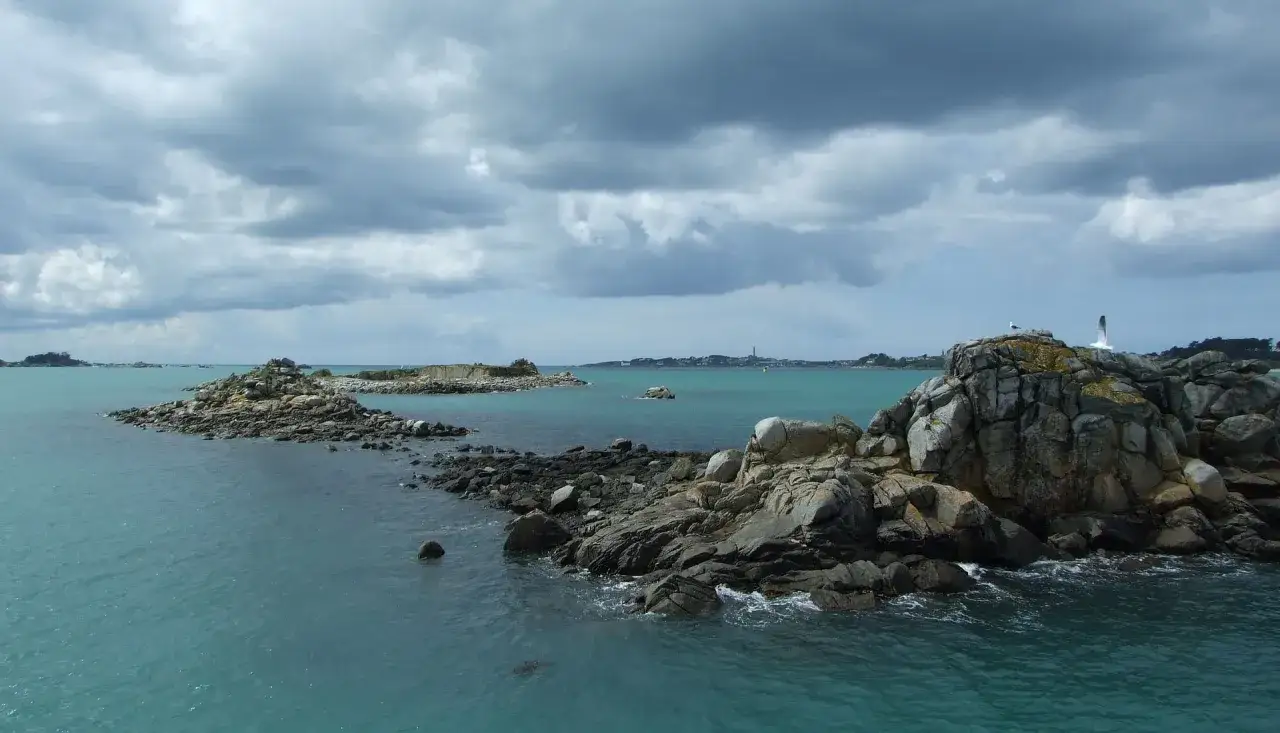 Vue sur la mer turquoise pr&egrave;s de Douarnenez, avec des &icirc;lots rocheux et des mouettes. Le ciel est couvert, annon&ccedil;ant peut-&ecirc;tre un temps plus frais &agrave; la Pointe du Raz.