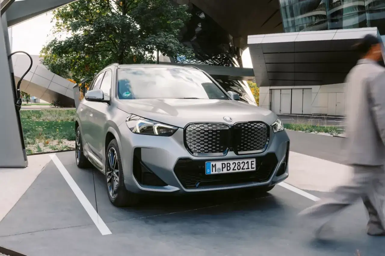 Srebrny BMW iX1 zaparkowany przy stacji ładowania, gotowy na podróż.