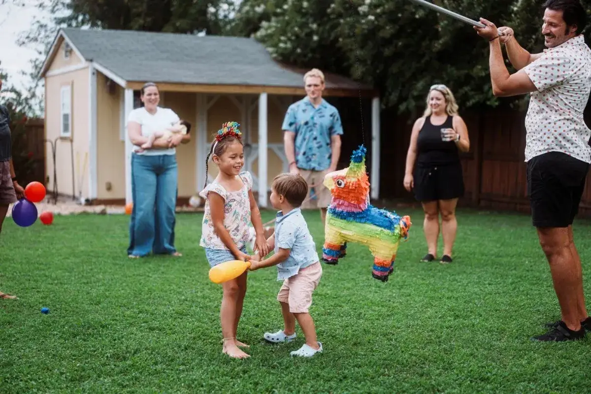 Ein bunter Piñata-Esel hängt im Garten. Ein Mädchen und ihr kleiner Bruder halten sich an den Händen, ihre bruder und schwester liebe ist spürbar.