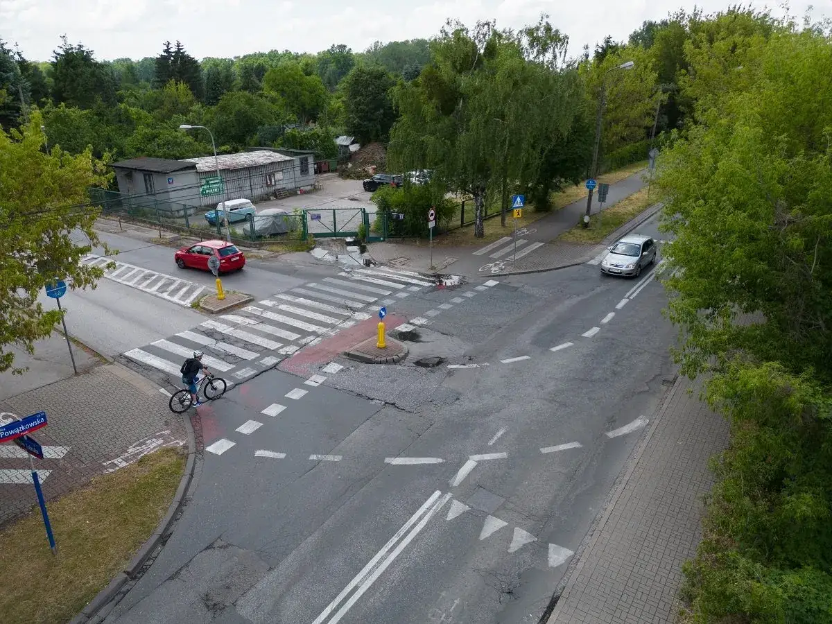 Rowerzysta zbliża się do wjazdu na rondo, gdzie czerwony samochód czeka na zielone.