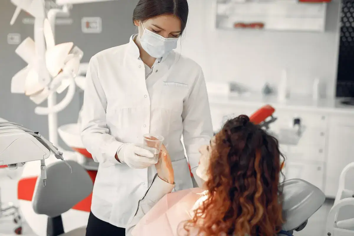 Dentystka w masce podaje wodę pacjentce. Bezpieczne leczenie kanałowe w ciąży jest możliwe.