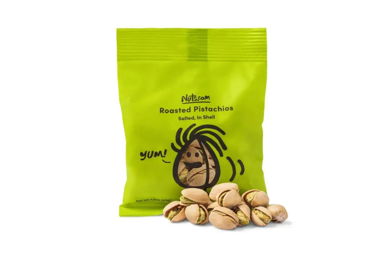 Grüne Tüte mit gerösteten Pistazien von Nuts.com. Ein paar Pistazien liegen davor. Wie gesund sind Pistazien? Sie sind ein toller Snack!